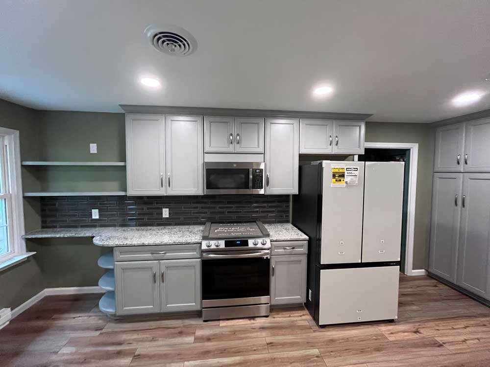 Kitchen with grey cabinets, granite countertops, a tiled backslash, and appliances