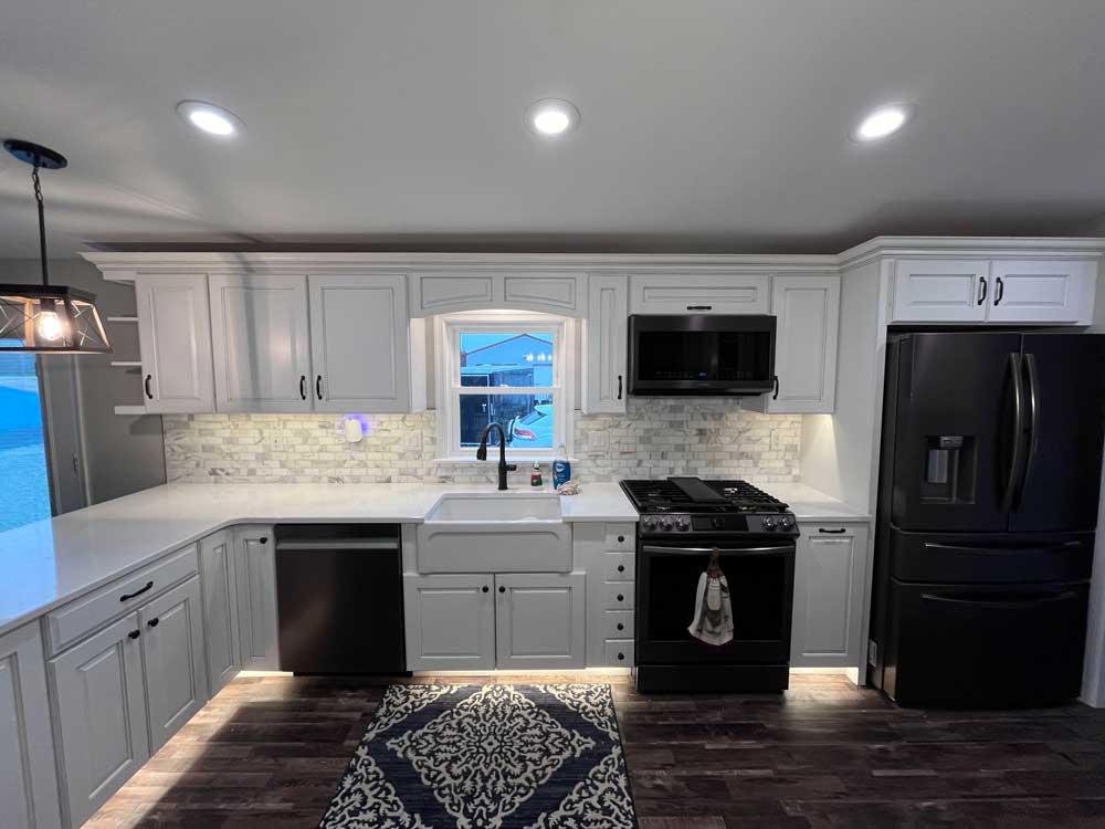Kitchen with white cabinets, under cabinet lighting, toe kick lighting, farm house sink, back stainless appliances, quartz countertops, a marble backsplash, and crown molding