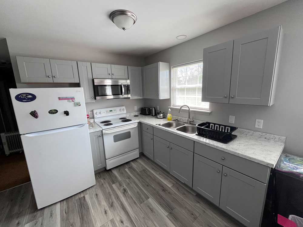 Grey kitchen cabinets, double stainless steel sink, countertops, and microwave.