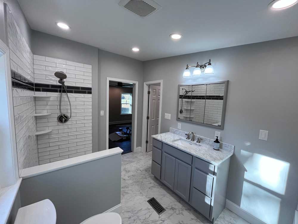Tiled bathroom including a vanity with a marble top, and a tiled shower with shelves