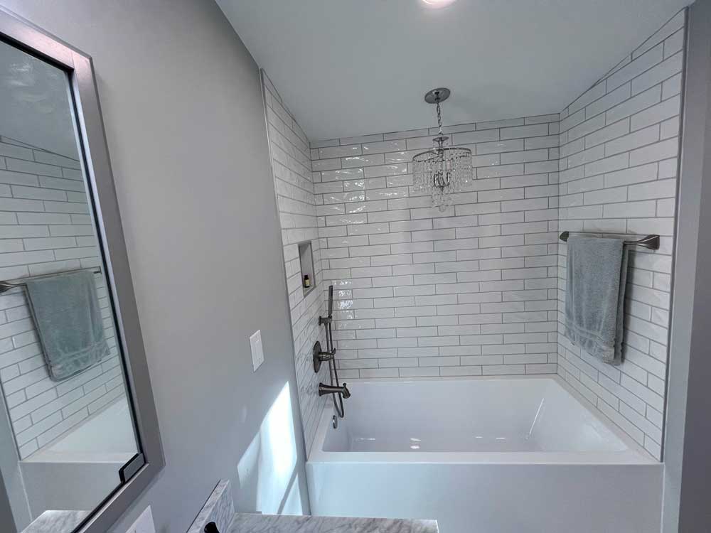 Tiled alcove bathtub with a towel bar, chandelier, tiled niche, and spray hose